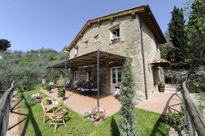 Une maison en pierre dotée d’un patio couvert, d’un espace salon extérieur et d’un jardin.