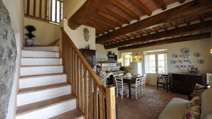 Un vaste espace de vie comprenant un escalier en bois, une table à manger avec des chaises, un canapé et un coin cuisine équipé d’un réfrigérateur et agrémenté d’assiettes décoratives accrochées au mur.