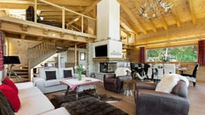 A spacious living area with a fireplace, leather sofas, a staircase, and a large window offering a view of the outdoors. - Chalet Charbray - Jacuzzi - Sauna - Views - La Tzoumaz, 4 Vallees (La Tzoumaz)