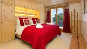 A bedroom with a wooden ceiling, a large bed with red bedding, and a sliding glass door leading to a balcony. - Chalet Charbray - Jacuzzi - Sauna - Views - La Tzoumaz, 4 Vallees (La Tzoumaz)