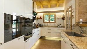 A modern kitchen with white cabinetry, granite countertops, and a wooden ceiling. - Chalet Charbray - Jacuzzi - Sauna - Views - La Tzoumaz, 4 Vallees (La Tzoumaz)