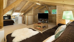 A cozy attic room with a wooden ceiling, a flat-screen TV, a sofa, a coffee table, and a lamp. - Chalet Charbray - Jacuzzi - Sauna - Views - La Tzoumaz, 4 Vallees (La Tzoumaz)