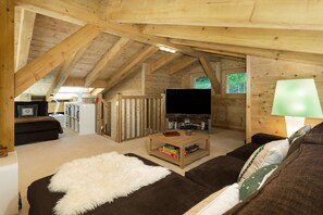 Ein gemütliches Dachzimmer mit Holzbalkendecke, einem Flachbildfernseher, einem Sofa, einem Couchtisch und einer Lampe.