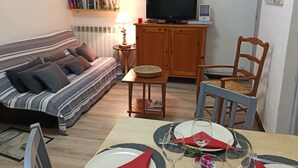 A cozy living room with a sofa, a dining table set for four, and a television. - Villa a few steps from the beach   (Saint-Cyprien)