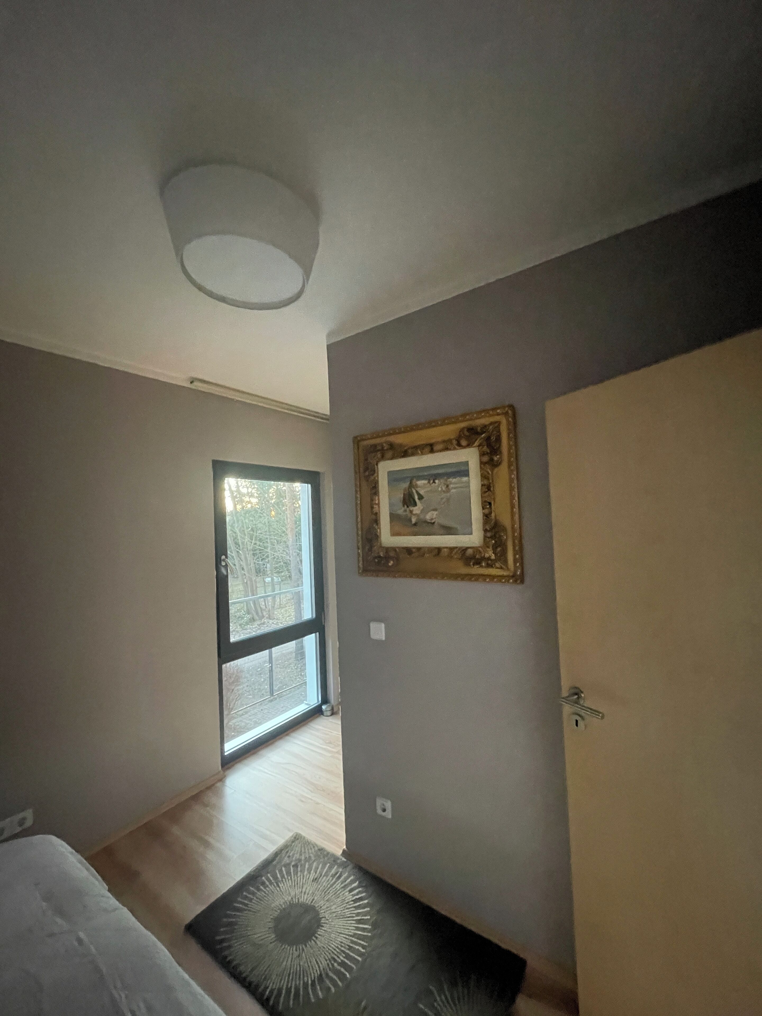 Une pièce avec une grande fenêtre, une porte et un tableau encadré au mur.