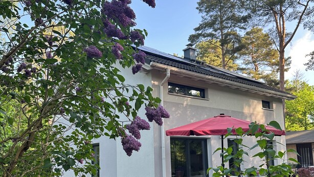 Ein weißes Haus mit roter Sonnenschirmterrasse, umgeben von üppiger Vegetation und Bäumen.