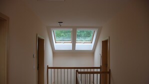 Ein Zimmer mit schrägem Dach, zwei Oberlichtern, einer Holztreppe und Blick ins Grüne.
