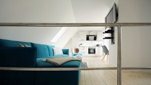 Una sala de estar moderna con un sofá color turquesa, una mesita de centro y una cocina al fondo.