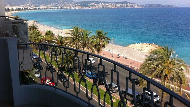 Un balcon avec vue sur une plage, des palmiers et une ville côtière en arrière-plan.