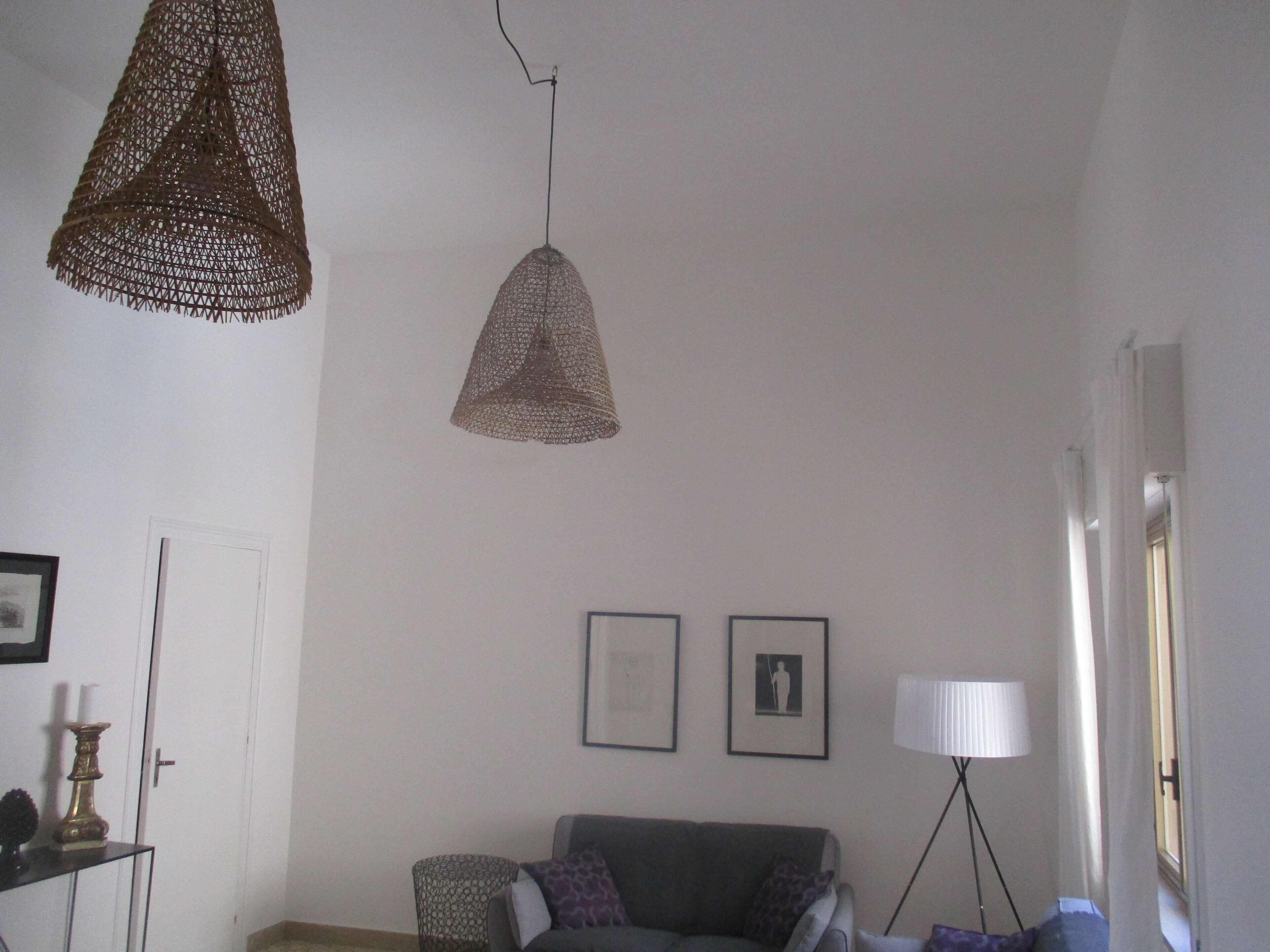 Un soggiorno con un divano grigio, due quadri appesi al muro, una lampada a sospensione intrecciata e una lampada da terra.