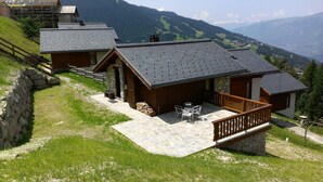 Un chalet doté d’une terrasse en pierre, d’un espace salon extérieur et offrant une vue sur les montagnes environnantes.