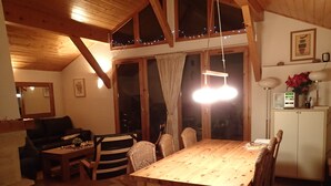 Un salon chaleureux avec une table à manger en bois, des chaises, un canapé et un téléviseur. Il y a une fenêtre avec des rideaux, un miroir et un meuble avec une lampe.