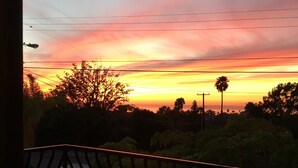 A balcony with a table and a chair, overlooking a sunset with trees and power lines in the background.