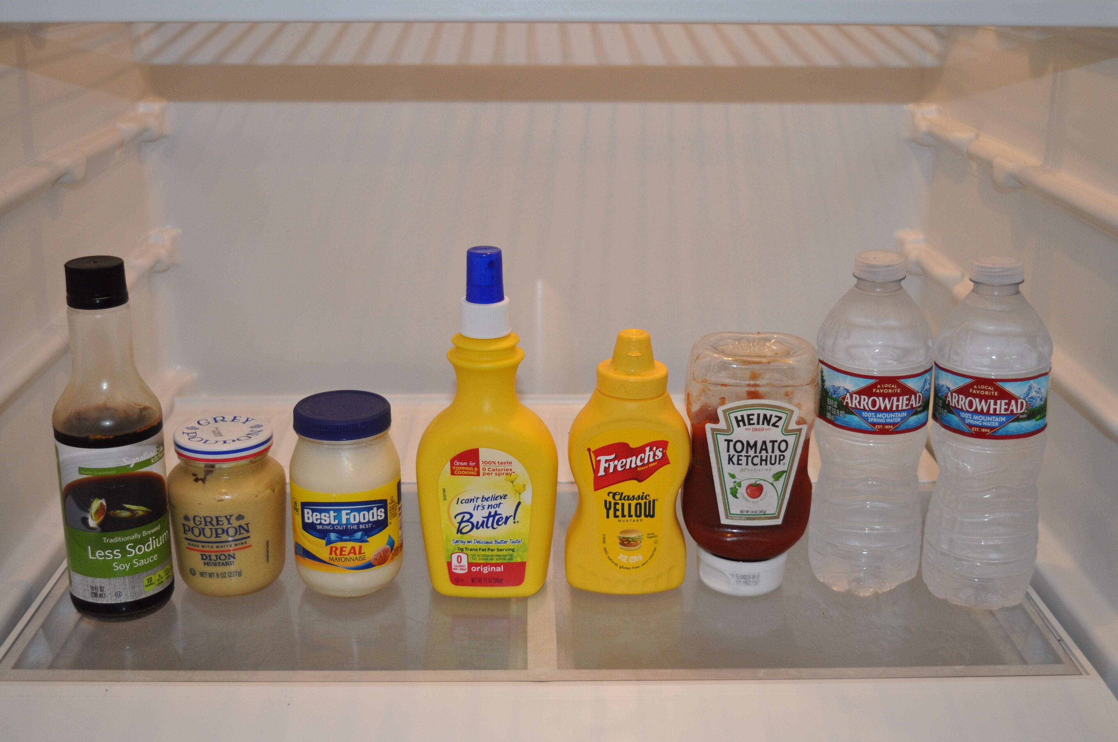 Ein Kühlschrankregal mit verschiedenen Gewürzen, darunter Sojasauce, Senf, Mayonnaise und Ketchup.