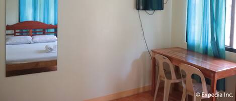 Una habitación con cama, televisión montada en la pared, una mesa de madera y una ventana con cortinas.