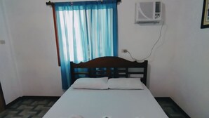 Una cama individual con estructura de madera, un control remoto y dos almohadas sobre un suelo estampado.