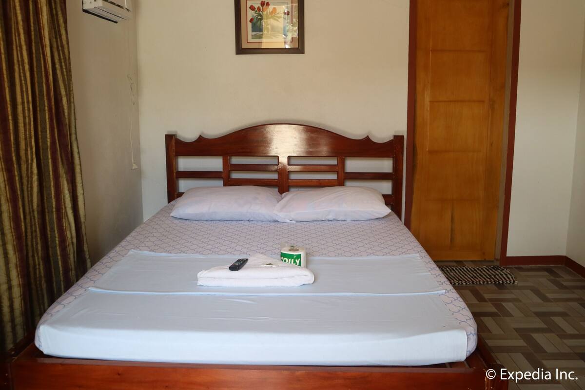 A neatly made bed with a white mattress, a wooden headboard, and a remote control on the bed.