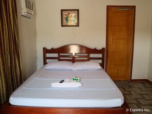 A neatly made bed with a white mattress, a wooden headboard, and a remote control on the bed. - Replica Manor (Siquijor)