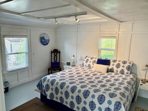 A bedroom with a bed, a chair, a nightstand, a lamp, a window, and a wall-mounted plate.