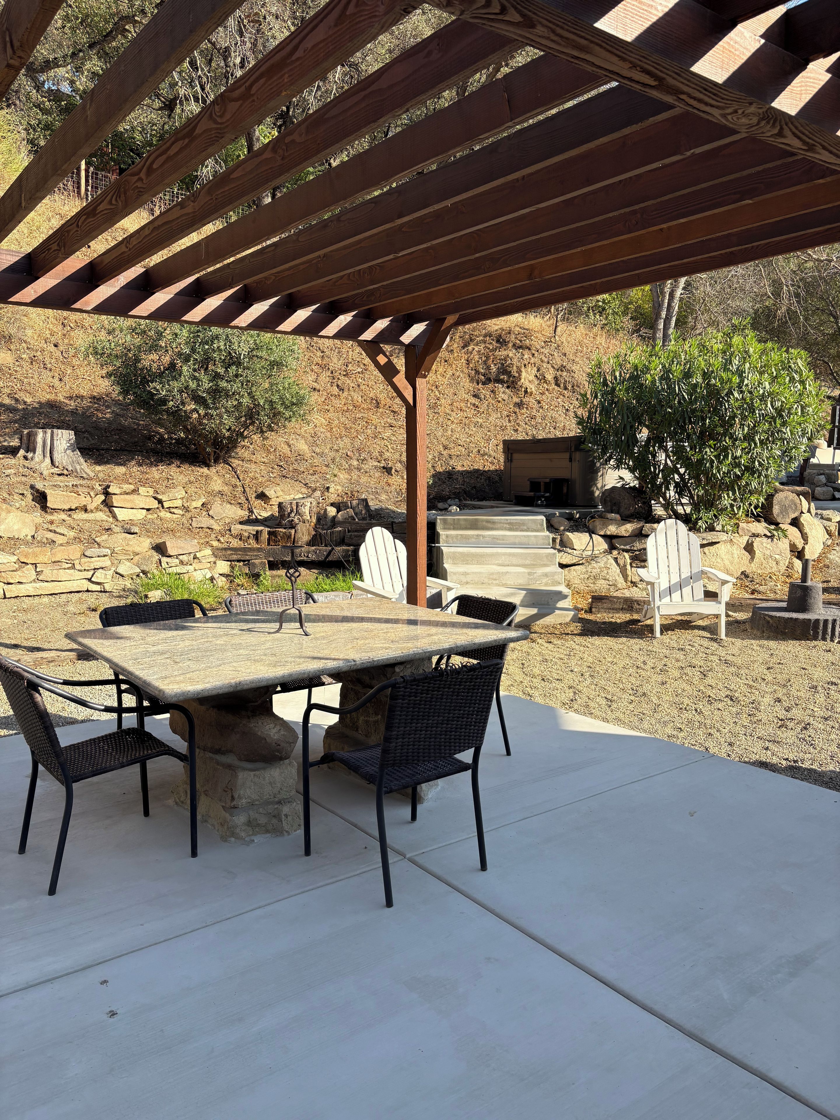 An outdoor patio with a pergola, stone table, and chairs.