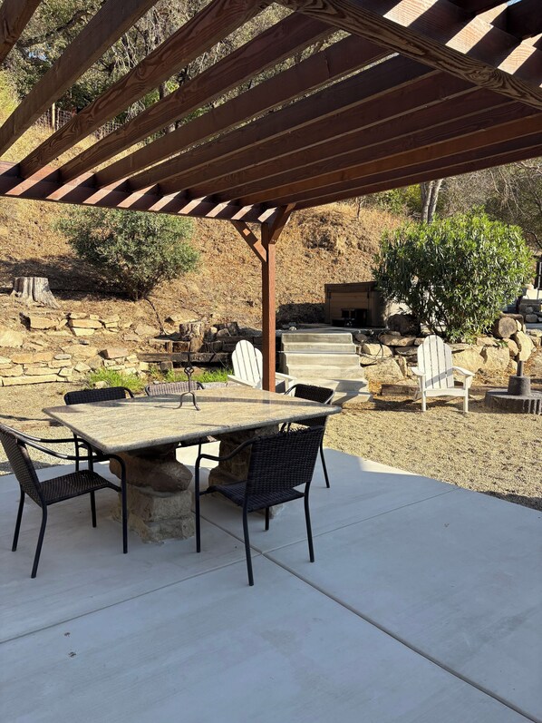 An outdoor patio with a pergola, stone table, and chairs.