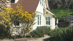 A two-story house with a stone chimney, a brown roof, and a gravel driveway. - Chic Historic Cottage in the Heart of 3 Rivers-close to SNP, Hot Tub, Love dogs! (Three Rivers)