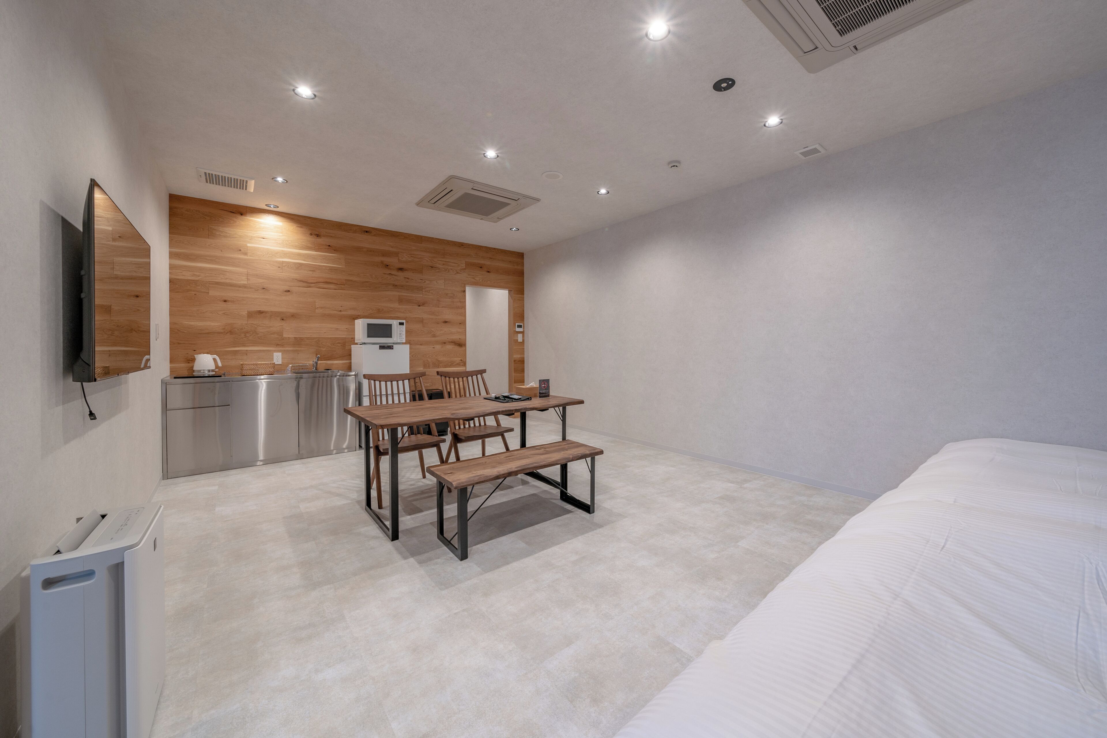 Una habitación de hotel moderna con una pared de acento de madera, kitchenette, zona de comedor con banco y una cama grande.