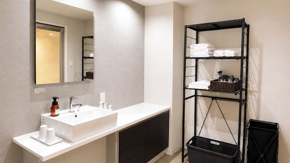 A modern bathroom with a white sink, a mirror, and a black shelving unit with towels and toiletries. - Relax Hotel Takayama Station (Takayama)