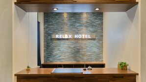 Un comptoir d’accueil surmonté d’une enseigne « Relax Hotel », un mur à texture et un plafond en bois.