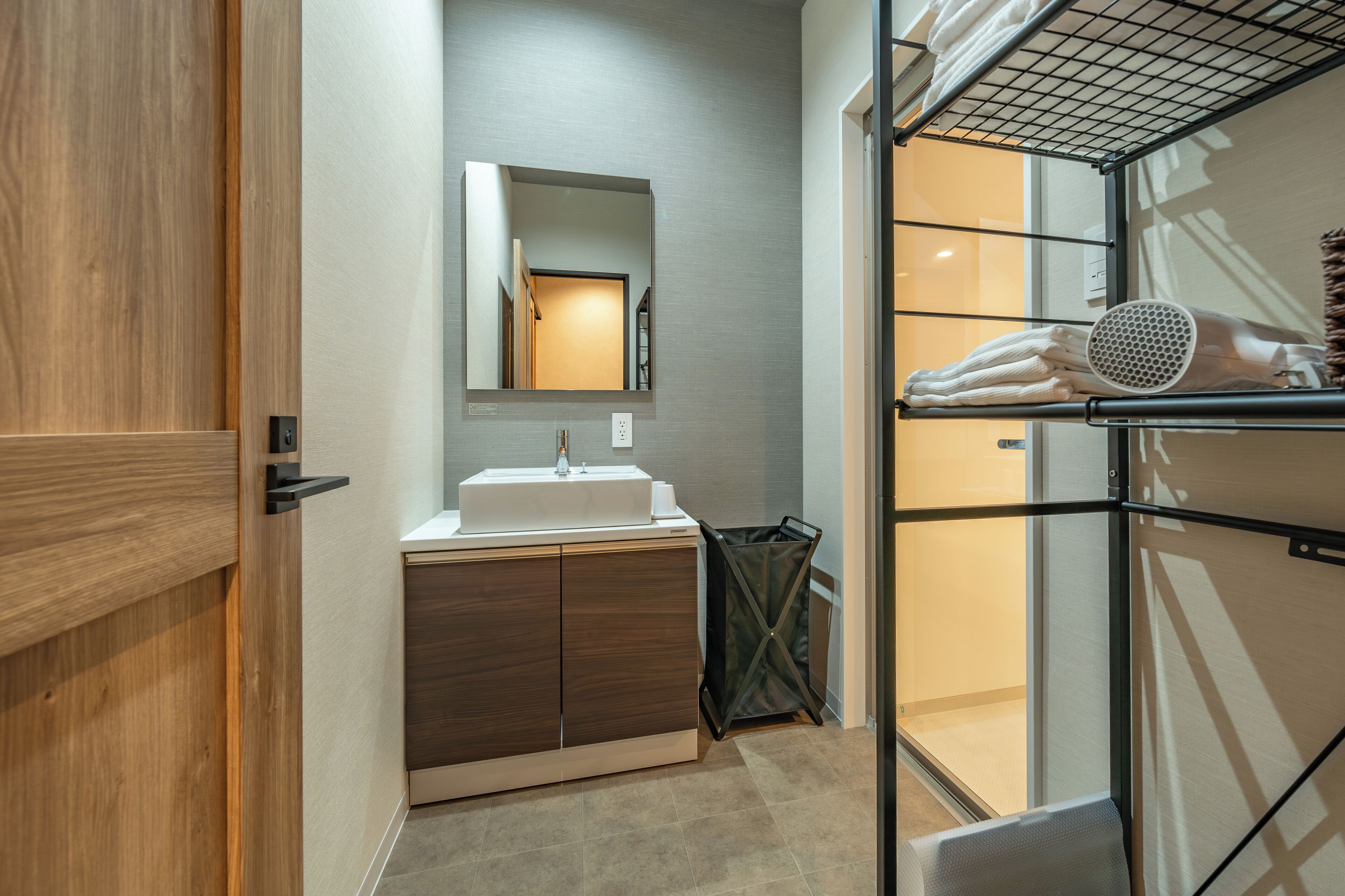 Un bagno moderno con una porta in legno, un lavabo, uno specchio e un portasciugamani con asciugamani e un asciugacapelli.