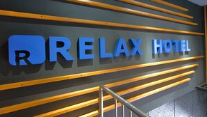 Un mur sur lequel est inscrit en grandes lettres bleues le texte « RELAYX HOTEL », et de part et d’autre duquel se trouvent des lattes de bois disposées horizontalement.