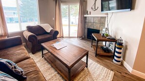 A living room with a sofa, coffee table, fireplace, and a television mounted on the wall. - 14-Plex Condo #114 Ground level, close to seasonal pool & spa (Garden City)