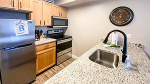 A compact kitchen with wooden cabinets, stainless steel appliances, a granite countertop, and a wall-mounted clock. - 14-Plex Condo #114 Ground level, close to seasonal pool & spa (Garden City)