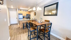 A dining area with a wooden table and chairs, a kitchen in the background, and a large mirror on the wall. - 14-Plex Condo #114 Ground level, close to seasonal pool & spa (Garden City)