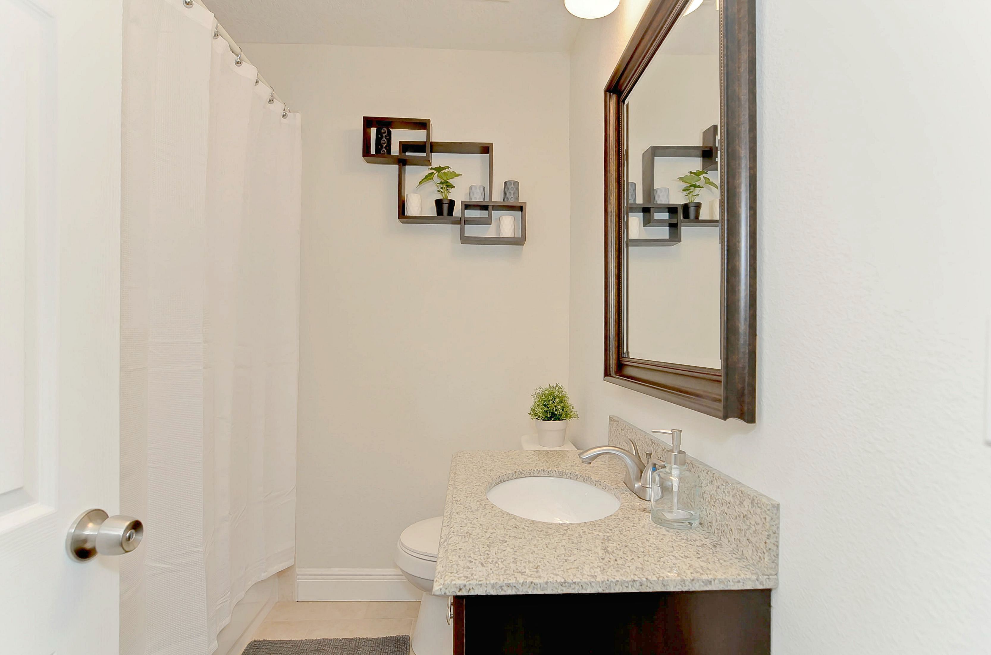 A bathroom with a white toilet, a sink with a mirror, and a shower curtain.