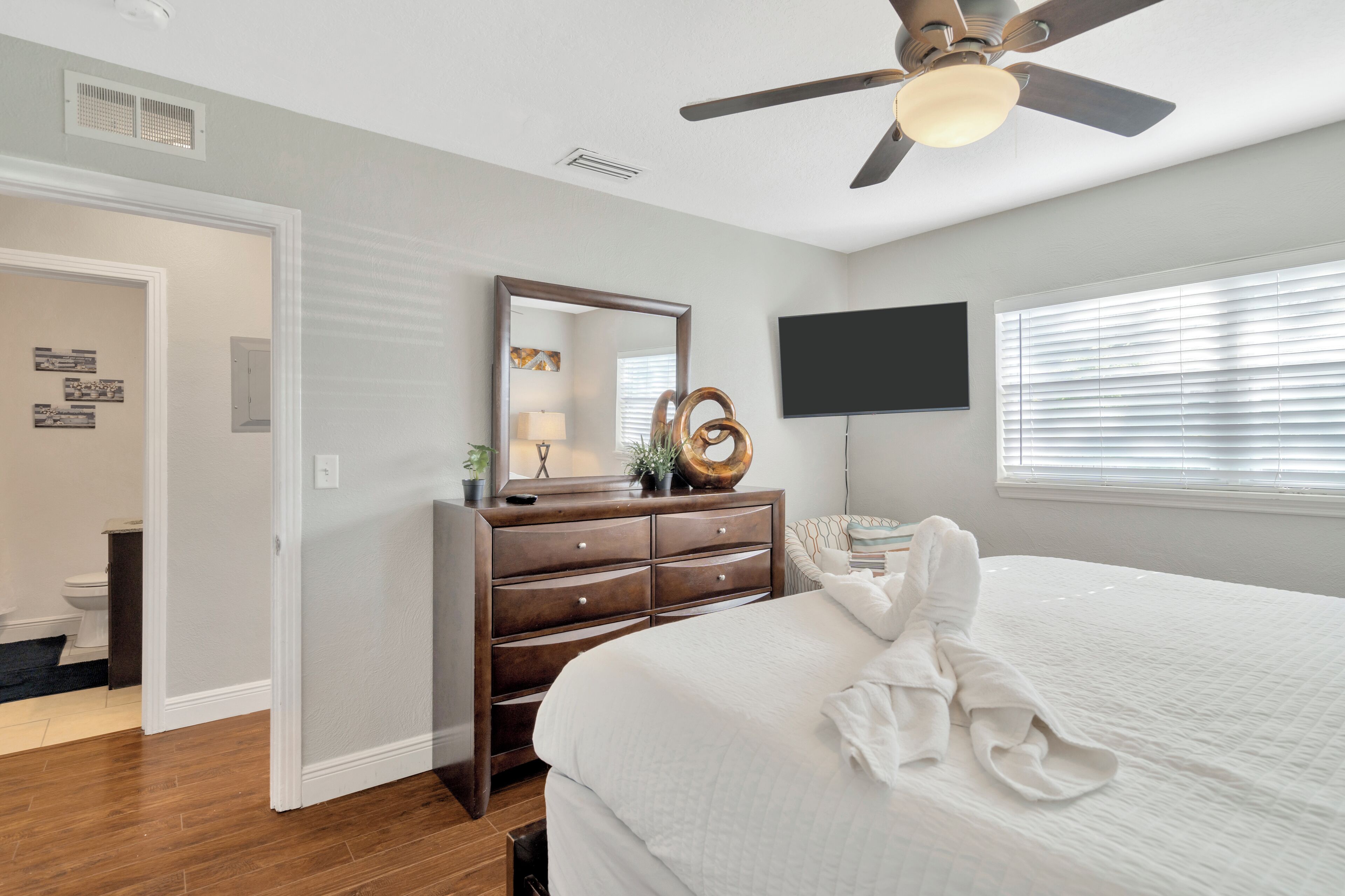 A bedroom with a bed, a dresser, a ceiling fan, a TV, and a window with blinds.