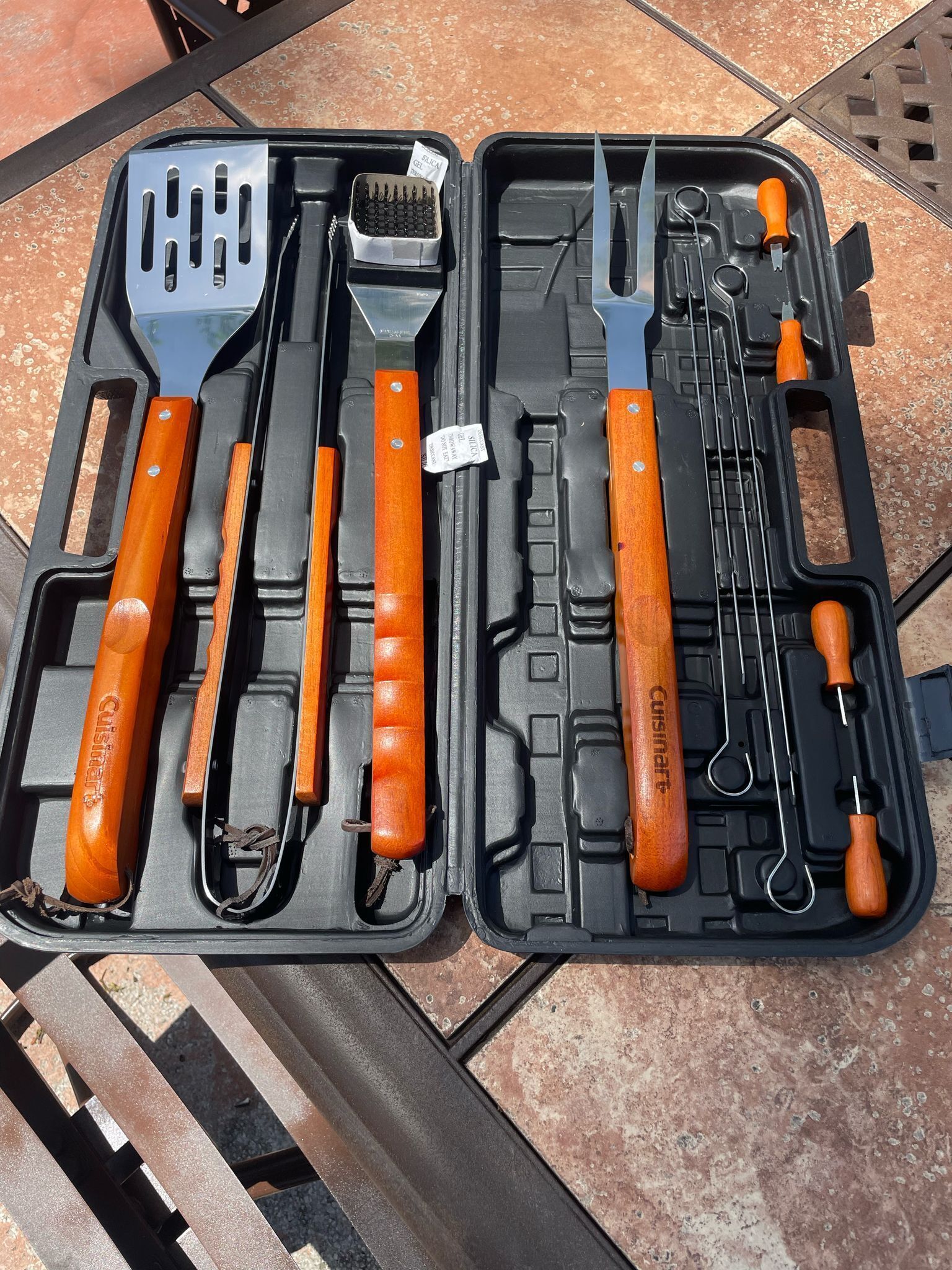 A black case with various kitchen utensils, including a spatula, tongs, and a grater, all with orange handles.