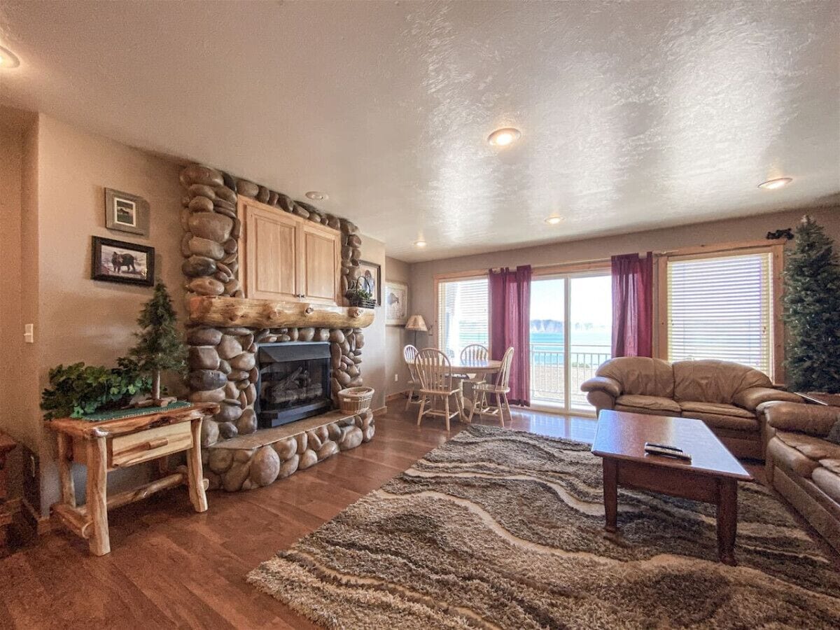 A living room with a stone fireplace, wooden furniture, and a view of the outdoors.