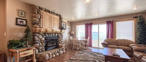 A living room with a stone fireplace, wooden furniture, and a view of the outdoors.