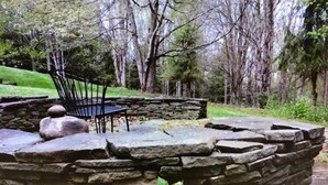 A stone bench with a metal frame, surrounded by a stone wall and greenery.