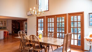 A dining area with a wooden table and chairs, a chandelier, and large windows with multiple panes.