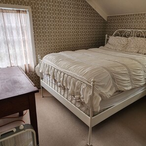 Une chambre à coucher avec un lit en métal blanc, un bureau en bois et un mur orné d’un motif.