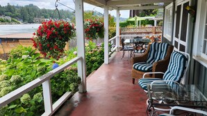 A covered porch with outdoor seating, a view of a body of water, and lush greenery.