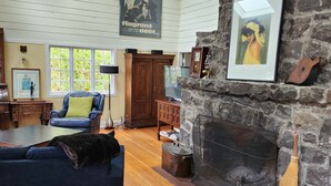 A cozy living room with a stone fireplace, wooden furniture, and a large window.