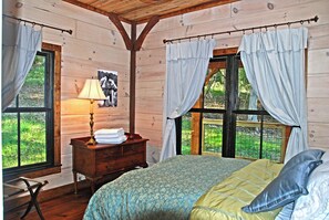 Quarto de cabana de madeira com cama, mesa de cabeceira, abajur e cortinas.