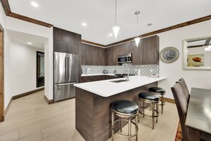 A modern kitchen with a central island, stainless steel appliances, and a dining area with a wooden table and bar stools.