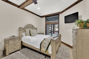 Un dormitorio con cama de madera, mesitas de noche, cómoda, televisor y ventana con vista al exterior.