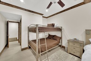 Ein Etagenbett mit Holz Kopfteil, ein Schminktisch und ein Deckenventilator in einem Zimmer mit weißen Wänden und Holzvertäfelung.