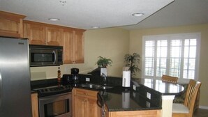 A kitchen with wooden cabinets, a stainless steel refrigerator, a microwave, an oven, a coffee maker, and a dining area with a round table and chairs.