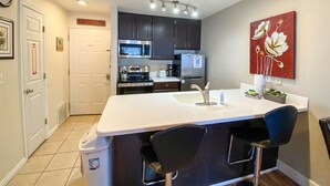 Una cocina compacta con encimera blanca, electrodomésticos de acero inoxidable y un pequeño comedor con dos sillas.